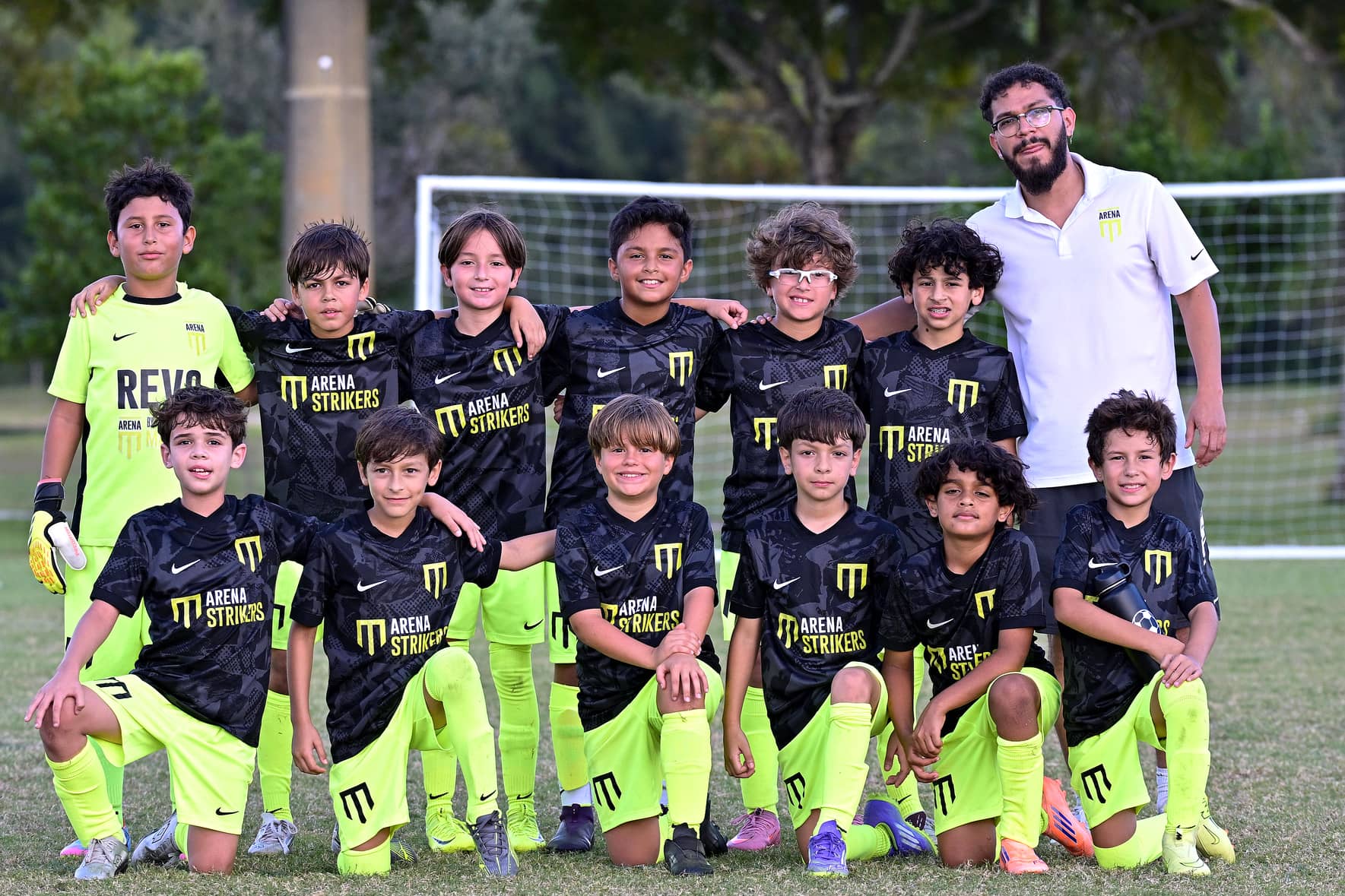 Arena Strikers youth team in black and lime kits posing with their coach for a team photo at a tournament