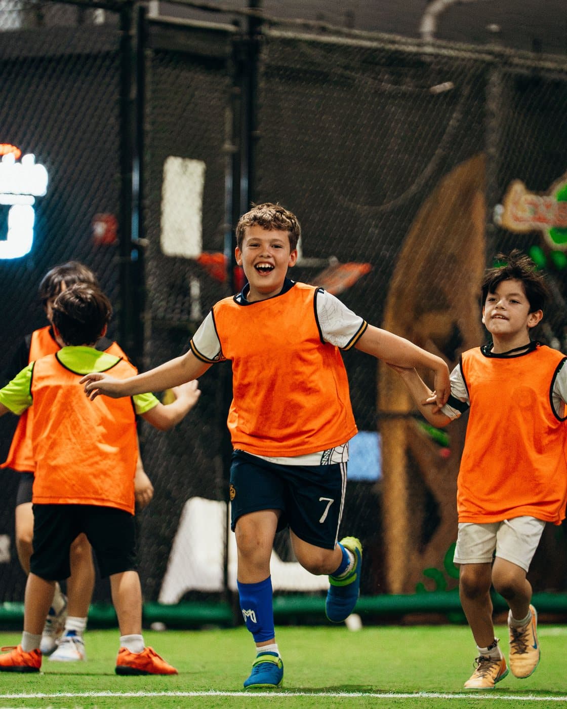 Campers in orange bibs running and laughing across the indoor field