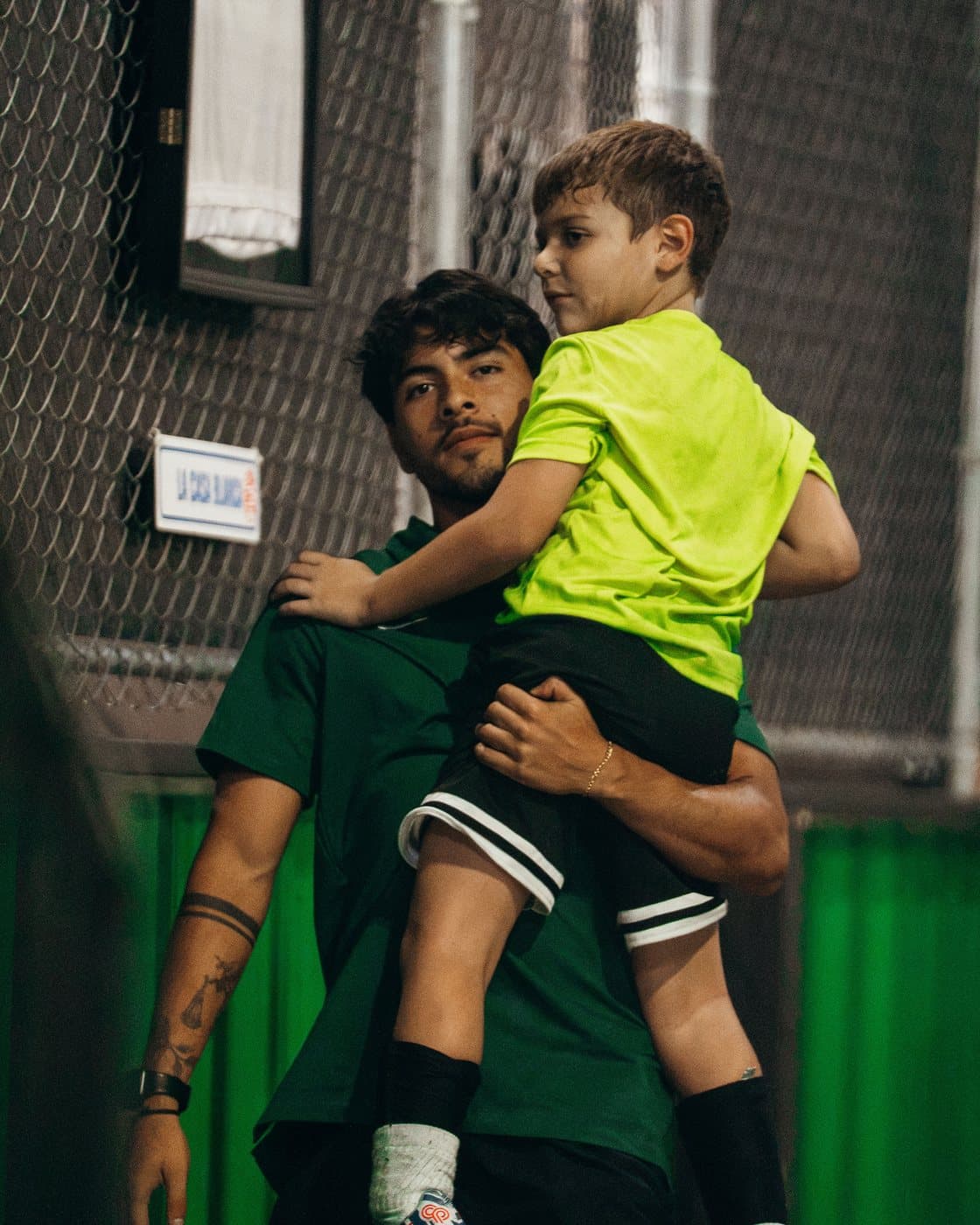 A coach in a green shirt carrying a young camper in a lime shirt at camp