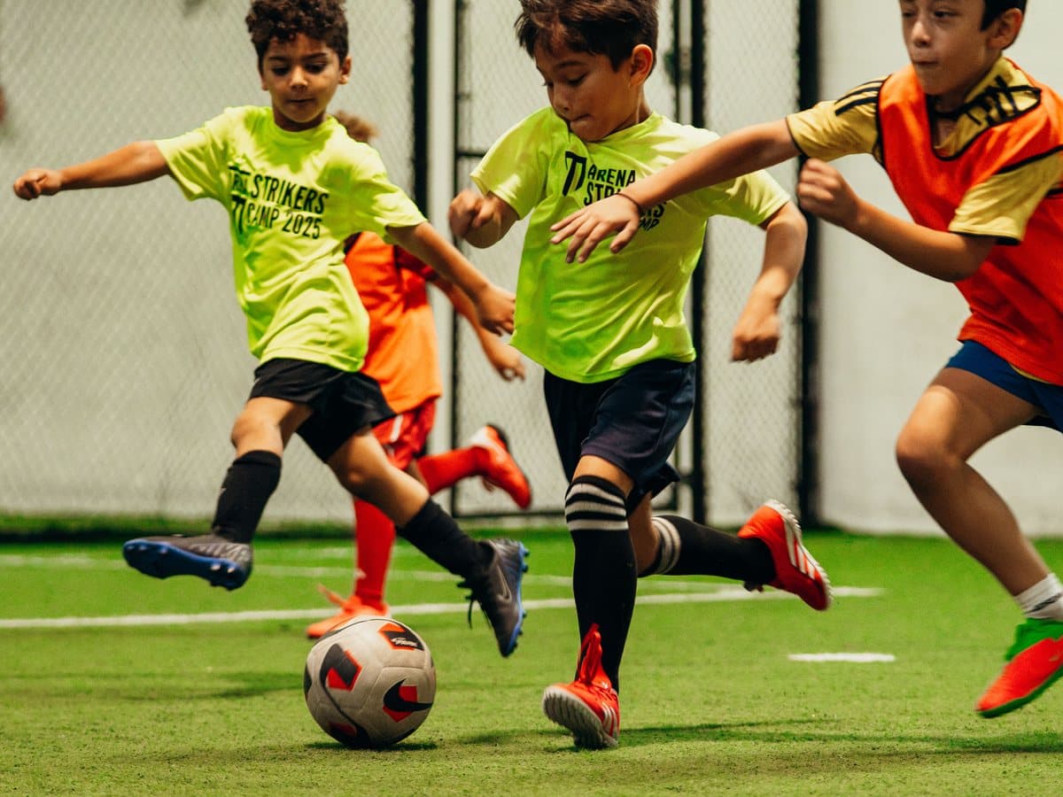 Campers in lime Arena Strikers camp shirts dribbling the ball on an indoor turf field