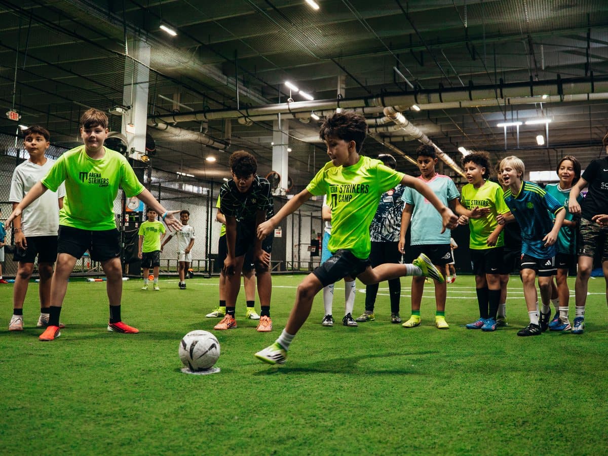 A camper shooting during a small-sided game while teammates watch on an indoor field