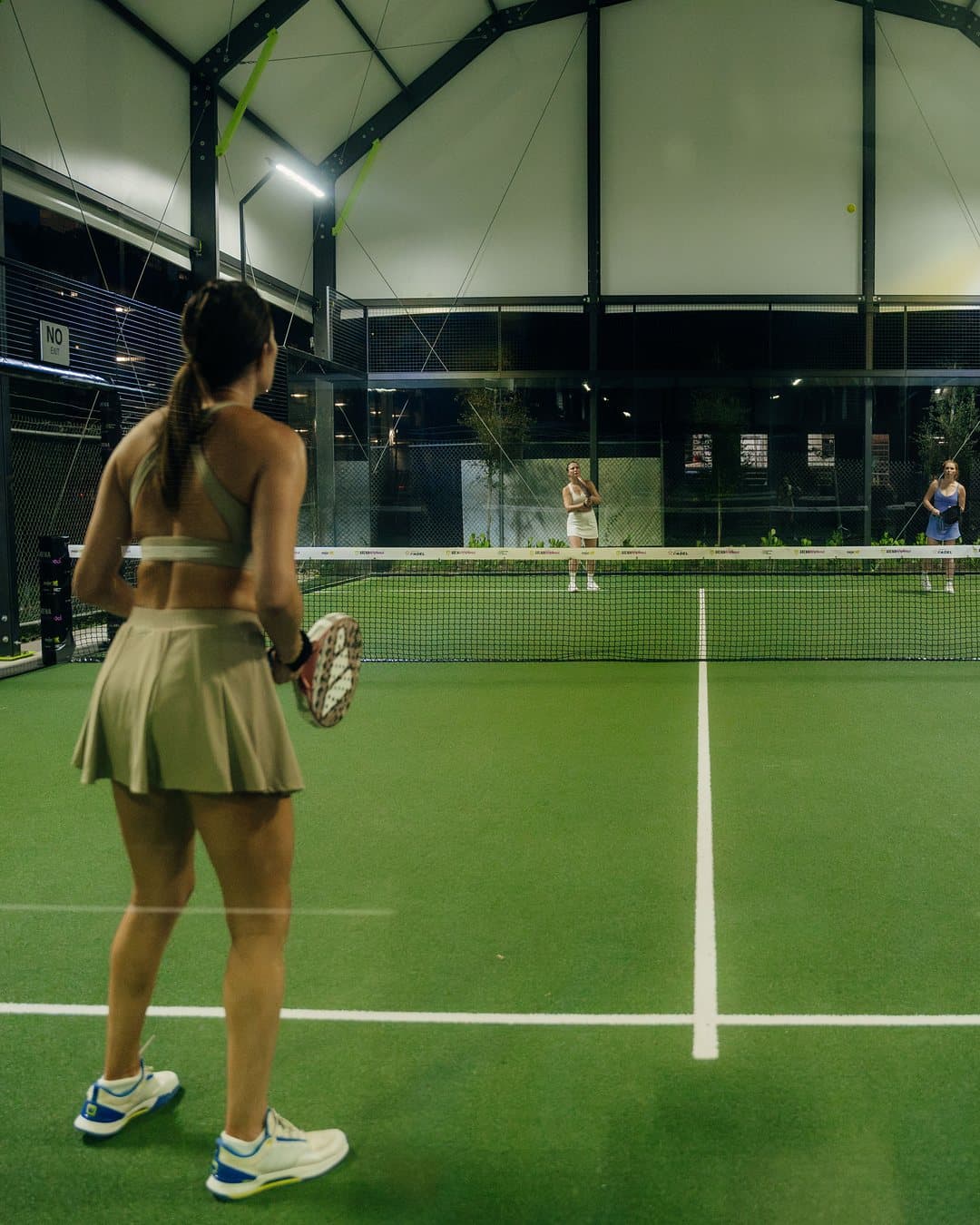 A doubles game on a covered padel court at Arena SSC Wynwood, Miami: a player waits at the baseline under the white roof