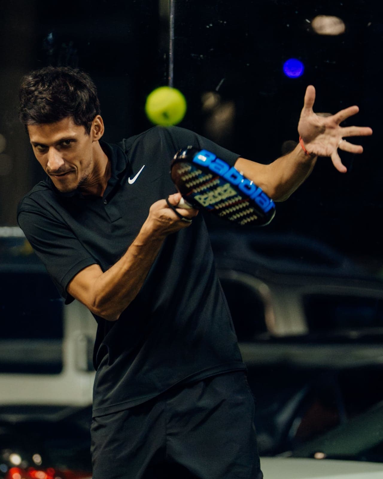 Padel player hitting a forehand volley, eyes on the ball, on a court at night at Arena SSC Wynwood, Miami