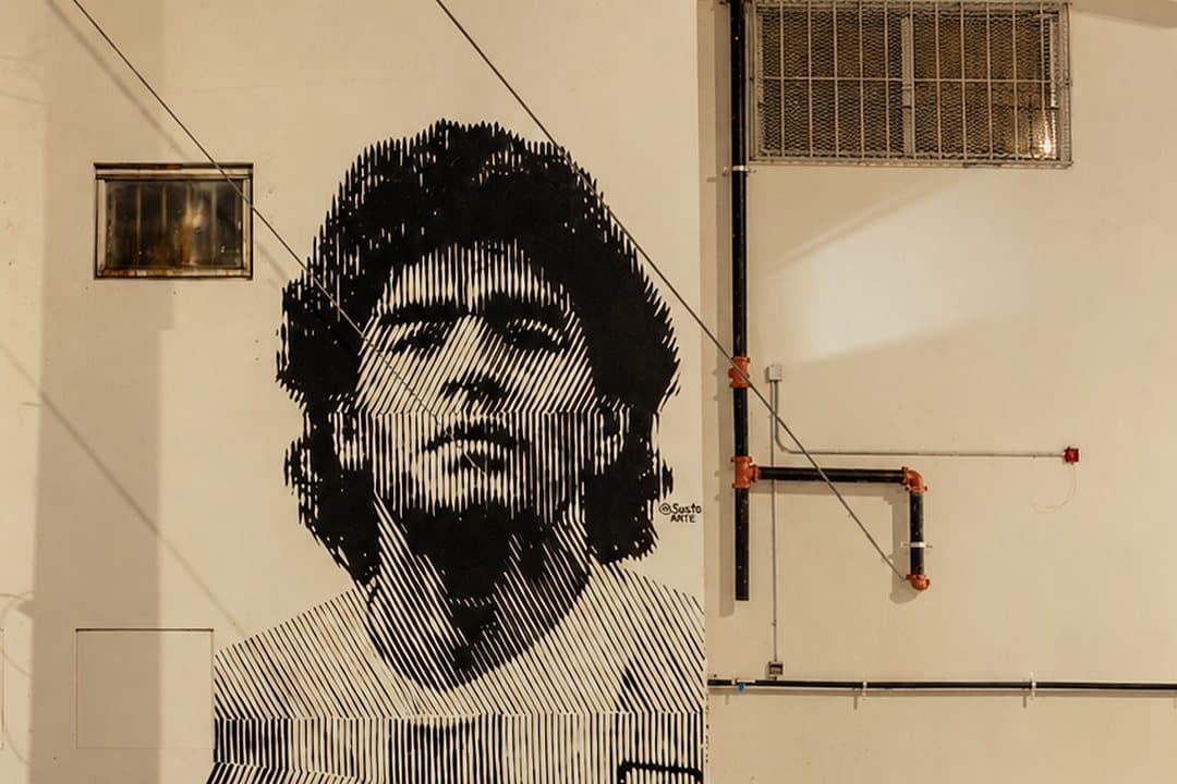 Black-and-white Maradona mural by @sustoarte on an outside wall of Arena SSC Wynwood at night