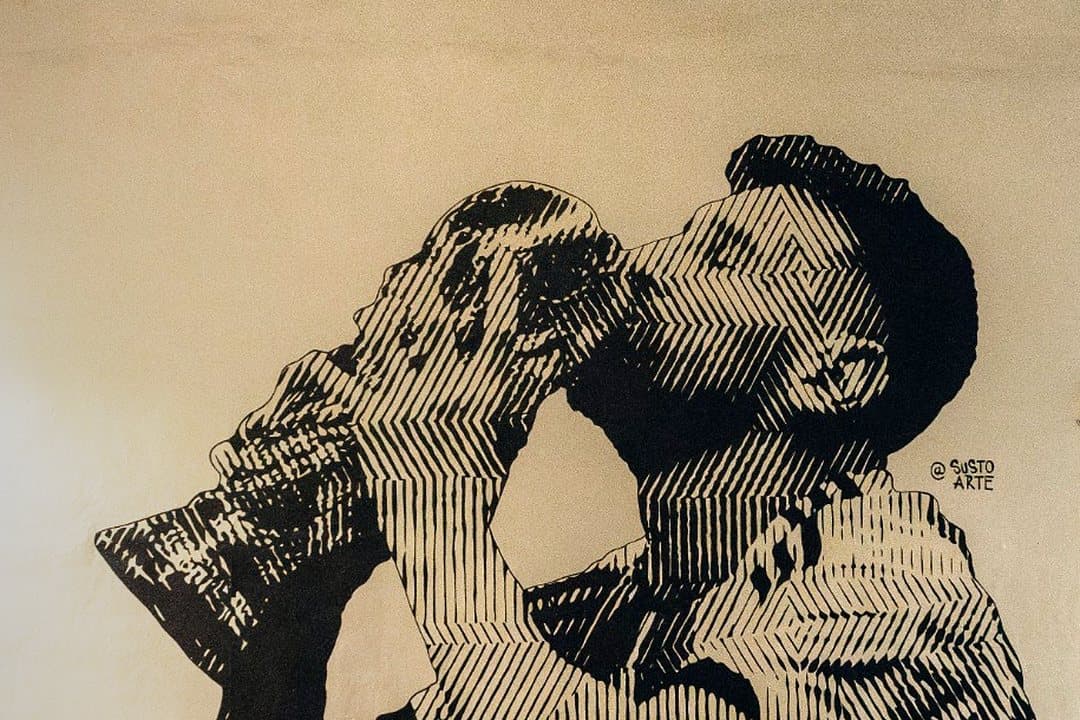 Black-and-white mural of Messi kissing a trophy, by @sustoarte, on an outside wall of Arena SSC Wynwood at night