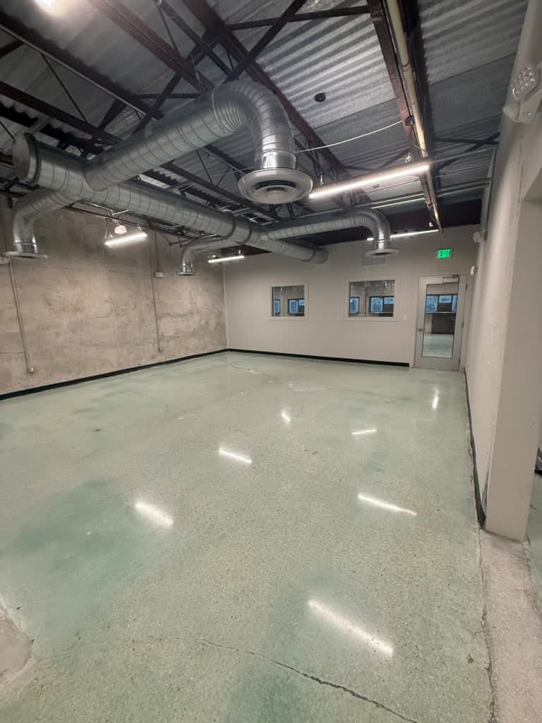 Party Room B at Arena SSC Wynwood, empty: polished concrete floor, exposed ducts and a glass door