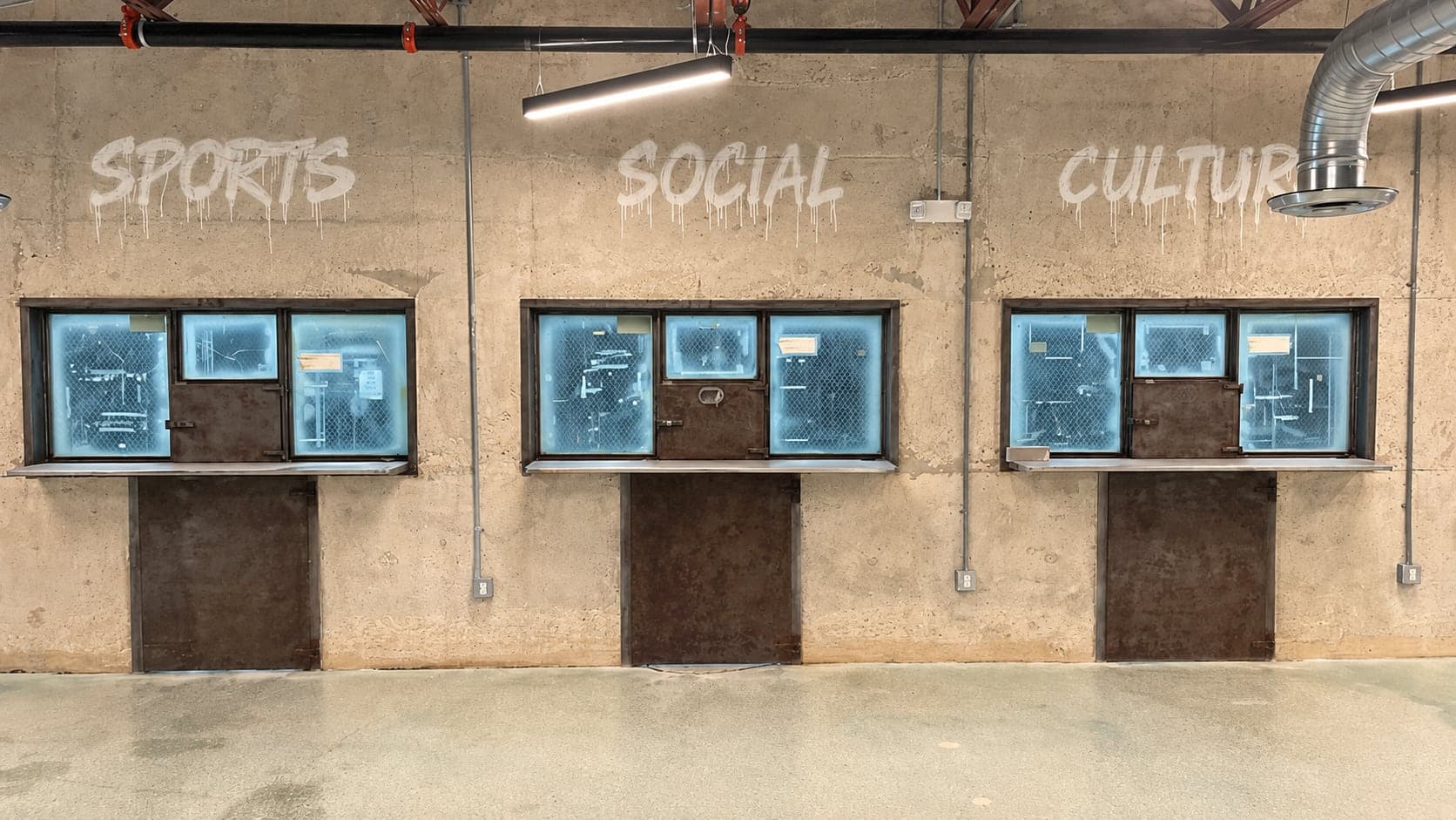 Concrete wall at Arena SSC Wynwood stenciled SPORTS SOCIAL CULTURE above three service windows