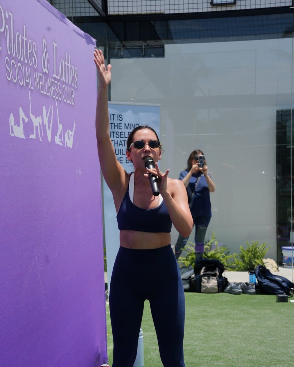 A pilates instructor leading the class with a microphone on an open-air padel court at Arena SSC Wynwood